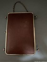 Back side of triptych mirror showing brown leather backing and metal chain for hanging