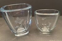 Two heavy vintage clear glass vases engraved with flower and butterfly motifs shown side-by-side