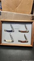 Framed set of four folding knives displayed with cardboard boxes behind