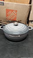 Grey round Le Creuset Dutch oven with lid and metal knob, Home Depot box background
