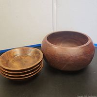 Four smaller real walnut salad bowls stacked and one larger walnut serving bowl arranged on a black tabletop.