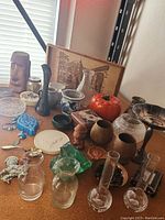 Angle showing various miscellaneous items including wooden mask, glass bottles, ceramic figurines, a framed etching, and metal bowl.