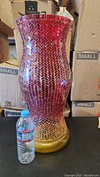 Image of tall mosaic glass vase in red and yellow with diamond pattern, next to water bottle for scale.