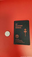 Front cover of 1942 WWII pocket missal showing title and author information next to a quarter for size comparison