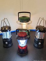 Front view of four outdoor lanterns, three black and one red, all lit except one black lantern that needs new batteries.