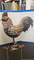 Full view of the large metal rooster yard decoration and three small metal yard stakes shaped like chickens and a rooster with paint wear and rust