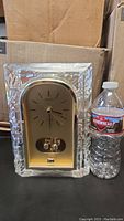 Front view of vintage Seiko quartz motion clock next to water bottle for size reference, showing clear textured case and gold clock face.