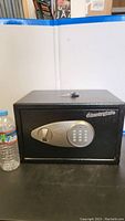 Black Sentry Safe with electronic keypad and key lock, two keys on top, water bottle on left for size reference.