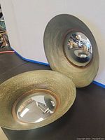 Two Uttermost wide round wall mirrors placed on a table, showing convex reflective surfaces and textured gold-bronze frames