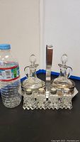 Vintage crystal salt and pepper shakers along with two glass vinegar and oil cruet bottles on a table, next to a water bottle for scale.