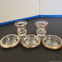 Front view of three sterling silver coasters with glass inserts and two glass toothpick holders with sterling silver lion-decorated rims.