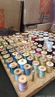Perspective showing rows of wooden thread spools with diverse pastel, green, blue, pink, and neutral colored threads on a wooden board.