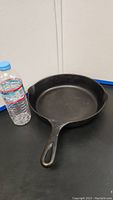 Side angle of black cast iron skillet with handle and water bottle for scale