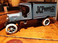 Side angle of blue and black die-cast 1925 Kenworth truck coin bank with JC Penney Co. branding and white wheels on wood surface.