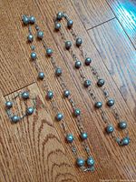 Photo showing two long antique sterling silver bead necklaces and one matching bracelet laid flat on wood floor.