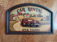 Frontal view of handcrafted wooden sign with dimensional red vintage open tourer car on rural background, showing text 'Car Rental Open Tourer'.