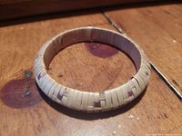 Top-down view of round woven bracelet showing detailed weaving pattern and natural materials on wooden surface.