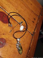 Photo of sterling silver and amber pendant on black cord necklace with antique sterling stick pin resting on a wooden surface.