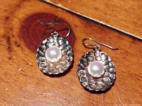 Close-up of two heavy sterling silver clamshell earrings with a central pearl on each, displayed on a wooden surface.