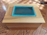 Top view of wooden keepsake box showing the glass inset with blue-tinted edges that allows viewing inside the box. Wood joins visible with dovetail construction.