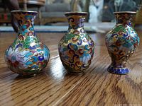 Three small Eastern Asian cloisonne vases showing floral and leaf patterned enamel with gold outlines