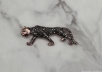 Bronze tone cheetah brooch decorated with black stones placed on a white marble surface.