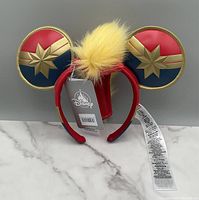 Front view of new Disney Marvel Captain Marvel padded ears headband with attached tags, showing star emblem on ears and yellow faux fur tuft on top.