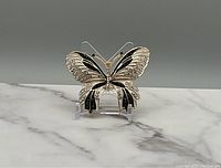 Front view of gold tone butterfly brooch with black enamel and clear stones on wings, displayed on clear stand over marble surface.