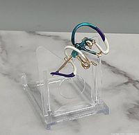 Side angled view of the gold tone twirler dancer brooch pin on clear stand, showing detailed enamel colors teal, purple, white, and gold tone metal.