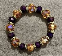Top-down photo of a circular bracelet with alternating gold-tone and purple faceted beads on a gray surface.