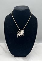 Front view of gold tone necklace with white bull pendant displayed on black jewelry stand.