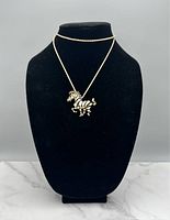 Gold tone necklace with zebra pendant displayed on a black necklace stand. The pendant features enamel black and white stripes, and the chain is fine gold-tone.