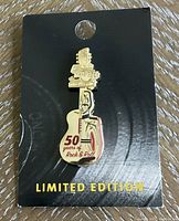 Gold-colored enamel Hard Rock 50th anniversary guitar silhouette pin mounted on original black card.