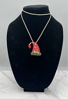 Photo of a gold tone necklace displayed on a black bust. The pendant is shaped like an elf hat in red and green with rhinestone accents and a red pom-pom, detailed with a pattern and small embellishments, can be used as a brooch.