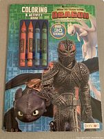 Photo of the front cover of How To Train Your Dragon Coloring & Activity Book with four markers and images of dragons and a character in armor.