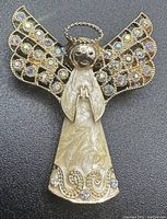 Front view of vintage Monet angel pendant pin showing detailed hammered gold-tone metal, multicolored rhinestones on wings and skirt, and halo loop detail.