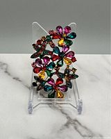 Front view of multicolor flower and leaf design brooch displayed on clear stand showing colorful faceted stones in gold-tone metal setting.