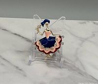 Front view of the gold tone dancer brooch with multicolor enamel and crystal-like stones on a display stand.