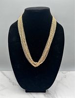 Multiple gold tone chain necklaces displayed on a black bust stand showing various chain link styles and lengths.