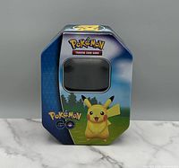 Front view of the Pokemon Trading Card Game collector tin featuring Pikachu with a window to show contents inside.