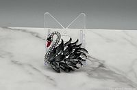 Front view of a silver tone swan brooch with black stones for wings and clear rhinestones on the neck, red beak accent.