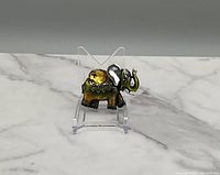 Photo of silver tone elephant brooch with green and yellow iridescent finish on clear acrylic stand over a marble surface