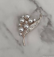 Gold tone brooch with pearl and rhinestone decoration on marble background, front view