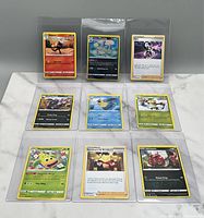 Photo of nine Pokémon trading cards arranged in three rows, each in clear protective sleeves.