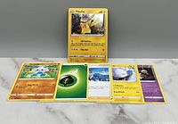 Six Pokémon trading cards displayed face up, including Pikachu with a crown, Makuhita, Leaf Energy, Wailmer, and two Shuppet cards.