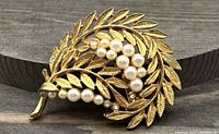 Photo showing vintage gold-tone swirl leaf brooch with faux pearl cluster detail on wood background