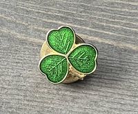 Close-up image of a small vintage gold tone shamrock pin with three green enamel heart-shaped leaves and gold leaf veining detail.