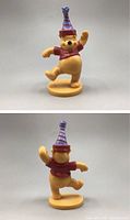 Front and back views of a vintage Winnie the Pooh figurine wearing a red shirt and purple striped birthday hat on a round yellow base.