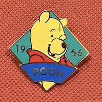 Photo showing an enamel collector trading pin of Disney's Winnie The Pooh with the year 1966 on a turquoise background and a blue banner with 'POOH'.