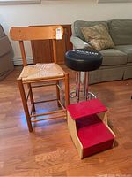 Tall wooden bar stool with woven seat and backrest shown beside shorter black cushioned bar stool and two-step wooden step stool